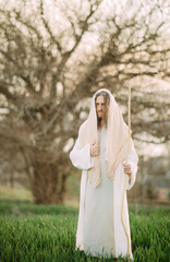 Wall Mural - Jesus Christ with wooden staff stands clothed in white robe against tree background.