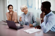 © Drazen - Senior CEO uses laptop and discussing with her younger co-workers during business meeting in  office.