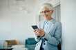 © Drazen - Happy senior businesswoman reads text message on mobile phone while works in her office.