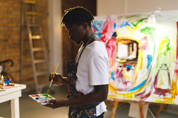 Wall Mural - African american male painter at work holding paints and brush in art studio