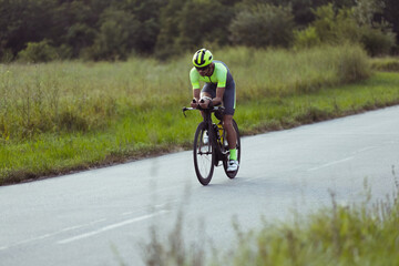 Wall Mural - Young male triathlete riding a bicycle on the open road. Professional sportsman is engaged in triathlon on bright summer day