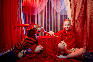 Young teenager girl during a stylized theatrical circus photo shoot in a beautiful red location. Young model posing on stage with curtain