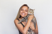 A Young Beautiful Smiling Blonde Woman Holds Young Tabby Cat In Her Hands Isolated On A White Background. Good Friends. Friendship Of A Pet And Its Owner. Cuddles