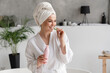 Caucasian young woman in bathrobe and spa towel eating cucumber while using beauty cosmetics for rejuvenation beautification moisturizing effect
