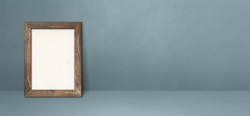 Wooden picture frame leaning on a grey wall. Horizontal banner