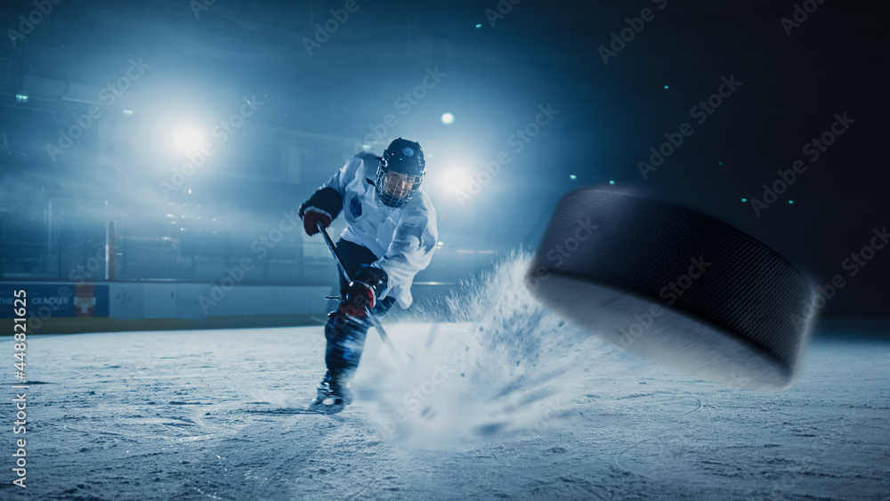 Ice Hockey Rink Arena: Professional Player Shooting the Puck with Hockey Stick. Focus on 3D Flying Puck with Blur Motion Effect. Dramatic Wide Shot, Cinematic Lighting. - obrazy, fototapety, plakaty 