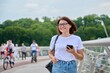 Portrait of middle-aged woman walking with smartphone in hand, summer day in city