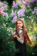 Wall Mural - Portrait of a cute schoolgirl in a school uniform among lilacs in spring