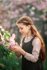 Wall Mural - Portrait of cute schoolgirl in school uniform looking at branches of lilac in spring