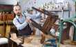 Portrait of furniture restorer inspecting antique armchair for restoration in workshop