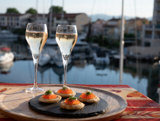 Russian style party with two glasses of white cold champagne, bliny with red caviar and view on Port Grimaud near Saint-Tropez in summer