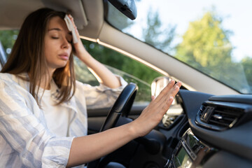 Woman driver has problem with a non-working conditioner, hand checking flow cold air, being hot during heat wave in car, suffering from summer hot weather, wipes sweat from her forehead with tissue. 