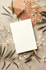 Invitation or greeting card mockup with envelope, eucalyptus and gypsophila twigs. Card mockup with copy space on beige background.