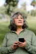 © McKinsey Jordan/Stocksy - Older Woman Holds Her Phone While Standing in the Park