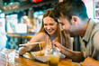 © Jimena Roquero/Stocksy - Young couple sharing Asian food in food court