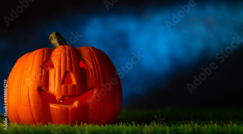 Fantasy mystical composition for the traditional autumn holiday Halloween. A large pumpkin in the form of a head with a creepy smile on the green grass against the background of the night cloudy sky.