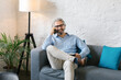 © Mihajlo Ckovric/Stocksy - Senior businessman sitting at the couch in the office using his mobile phone