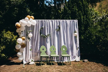 View of wedding decorations with balloons and leaves with three green chairs in front of it