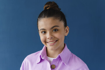 Wall Mural - Close-up view, positive teenage girl smiling beautifully, looking at camera. Cute little girl on a blue background