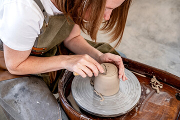 Woman working on the potter's wheel. Ceramist young woman making clay product on pottery lathe in studio. Close up of female hands working on potters wheel