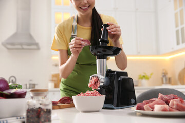 Poster - Young woman using modern meat grinder in kitchen, closeup