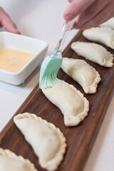 Sticker - Closeup shot of a male cook spreading sauce on uncooked dumplings on a long wooden board