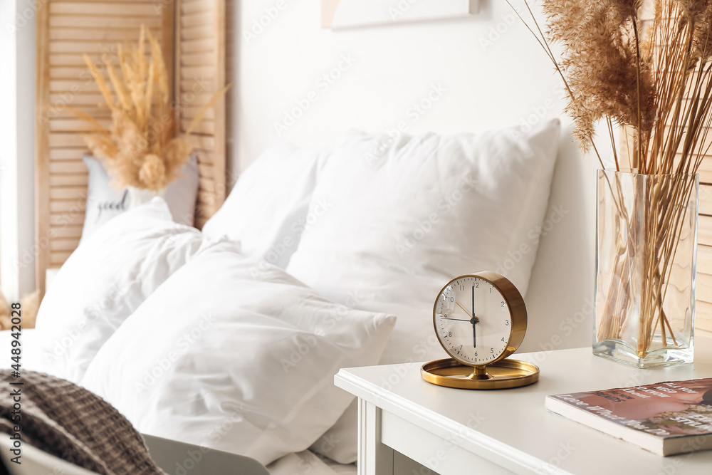 Stylish alarm clock on table in bedroom