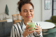 Young African-American Woman Drinking Fresh Smoothie In Kitchen