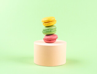 Geometric pastel green background with colorful macaroon sweet candies on circle podium