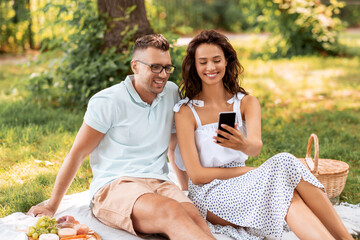 Poster - leisure and people concept - happy couple with smartphone having picnic at summer park