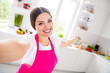 © deagreez - Photo portrait woman in pink apron smiling taking selfie showing her kitchen