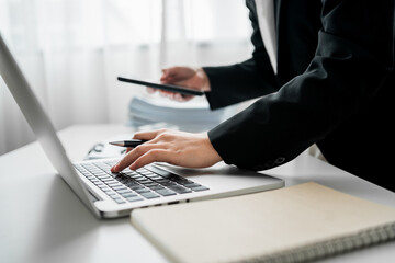 Canvas Print - Side view of Businesswoman using smartphone with laptop computer on a desk, female worker working multitasking, analyzing paperwork and business reports, financial and accounting concept.