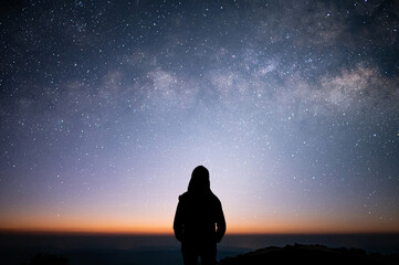 Wall Mural - Silhouette of young female standing and watched beautiful view sunrise, star and milky way alone on top of the mountain. She enjoyed traveling and was successful when he reached the summit.