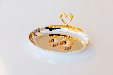 Wedding gold rings are lying on a yellow plate with a heart for a wedding.