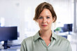 © sepy - Attractive businesswoman looking at camera while standing at the office.