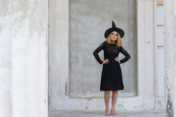 Full portrait of beautiful woman in black witch costume for halloween with hat on gray background