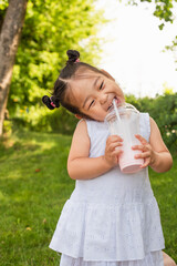 Canvas Print - happy asian toddler girl in dress drinking tasty milkshake in park