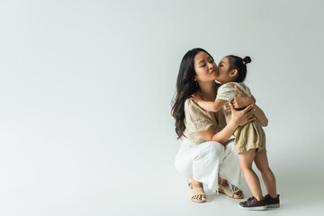 Wall Mural - full length of stylish asian mother hugging toddler daughter kissing her cheek on grey