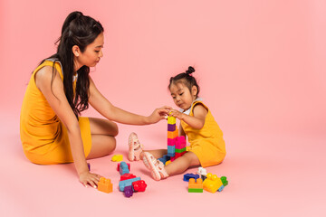 Canvas Print - asian woman and daughter sitting and playing building blocks on pink