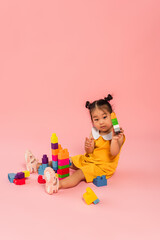 Canvas Print - brunette asian girl in yellow dress playing building blocks on pink