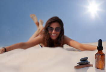 Glass bottle with a dropper for cosmetics - suntan oil. Blurry image Woman and vial on the beach