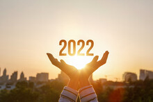 2022 Is Supported By Hands On The Background Of A Sunny Sunset.
