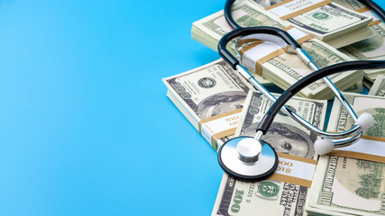 Profit driven hospital, premium medical insurance payment and high doctor bills expense concept with stethoscope, stacks of dollars and no people isolated on blue background with copy space