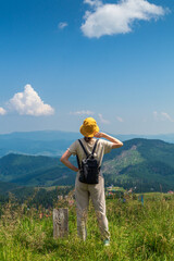 Wall Mural - Hipster traveler in hat and backpack resting in nature. A tourist girl looks at the panorama of the mountains. Mountain beautiful landscape