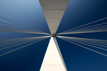 Minimalist Abstract Architecture Shot Featuring A White Concrete Pillar Of A Suspension Bridge With Two Bunches Of Suspension Cables Against A Clear Blue Sky