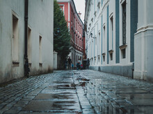 People In Narrow Passage Between Buildings, View From Behind, Streets After The Rain
