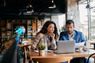 Business colleagues using laptop and analyzing documents on meeting in cafe.