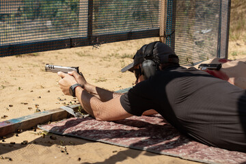 Wall Mural - Man in tactical clothes shooting from a pistol, reloading the gun and aiming at the target in the open-door Shooting range