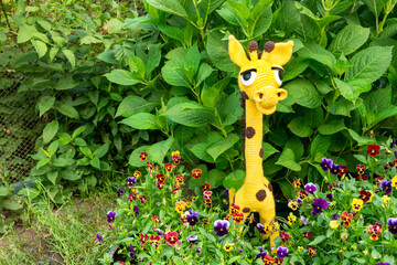 Wall Mural - Soft toy giraffe with a long neck amigurumi among the greenery of the garden.