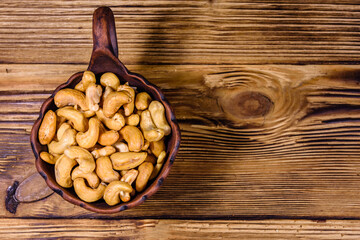 Canvas Print - Ceramic bowl with roasted cashew nuts on a wooden table. Top view